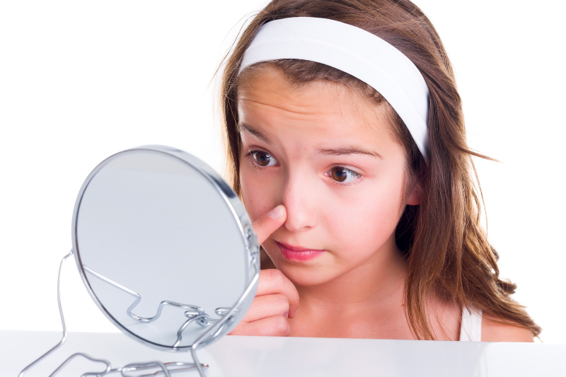young girl squeezing her pimple in a mirror